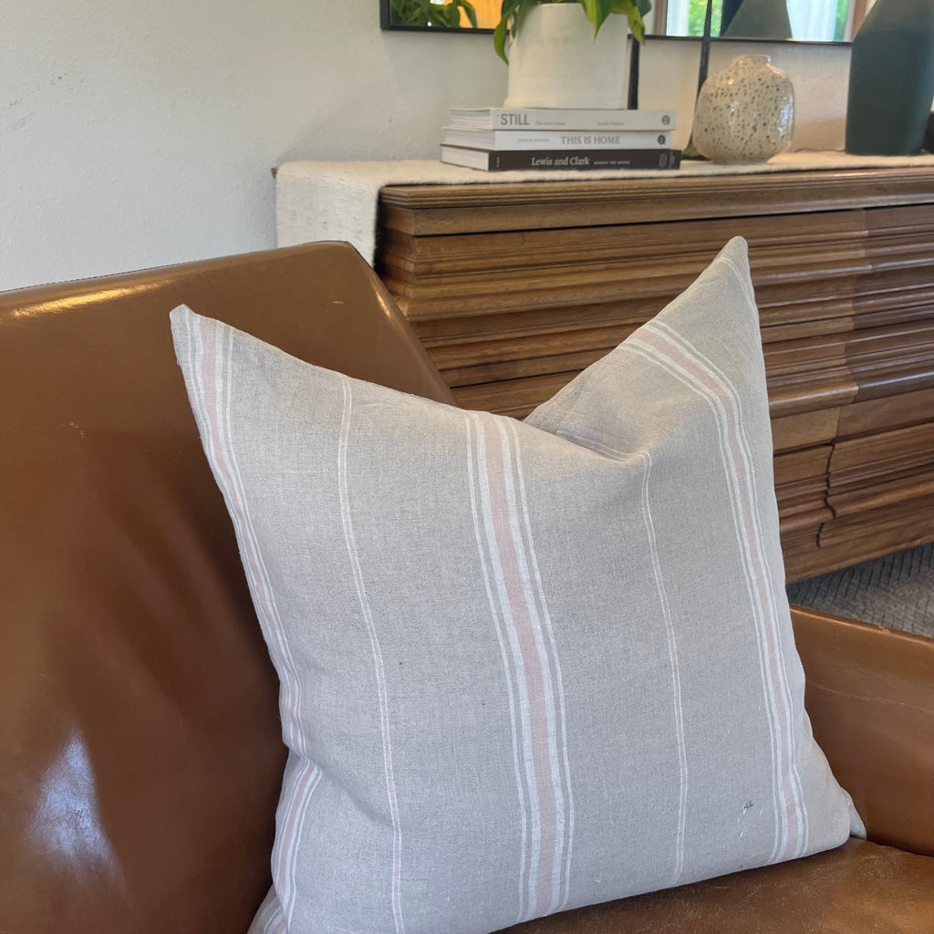 Pink, white, and tan striped linen pillow, paired with soft throws and neutral-toned decor. Three pillow sizes—20x20, 14x24, and 24x24—displayed together on a minimalist couch, showcasing variety and handcrafted quality.