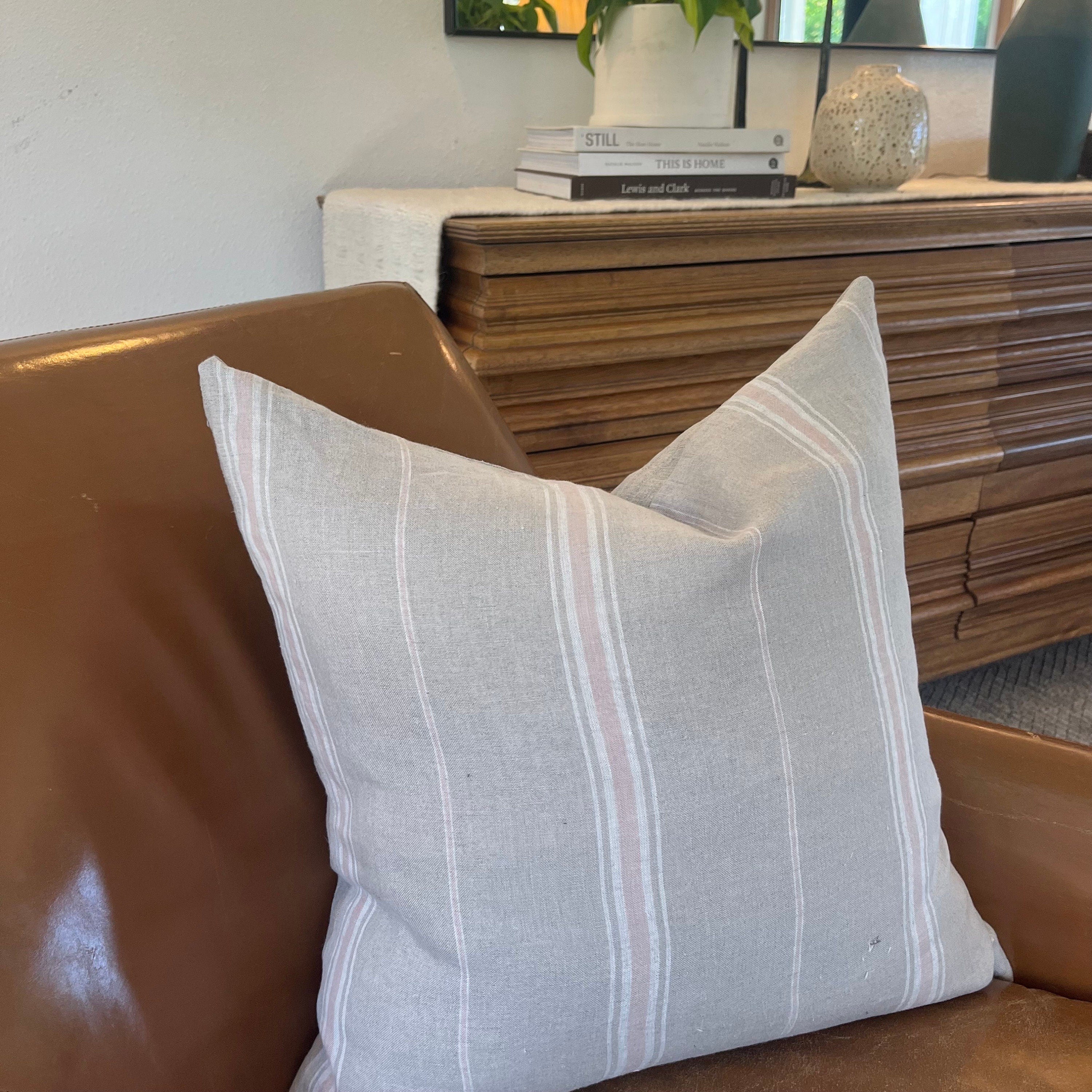 Pink, white, and tan striped linen pillow, paired with soft throws and neutral-toned decor. Three pillow sizes—20x20, 14x24, and 24x24—displayed together on a minimalist couch, showcasing variety and handcrafted quality.